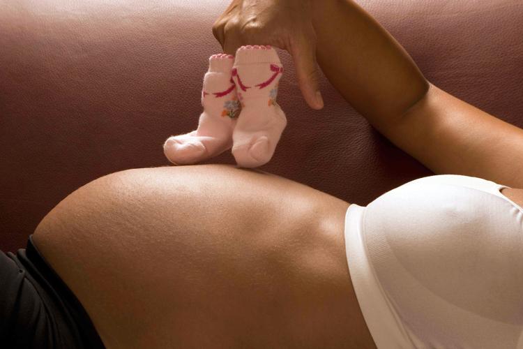 Pregnant woman holding pair of baby shoes - INFOPHOTO