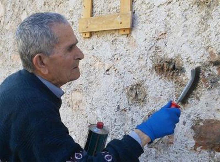 Il partigiano Enrico Angelini, mentre ripulisce il muro dalla svastica (Foto dal sito 'Foligno Oggi')