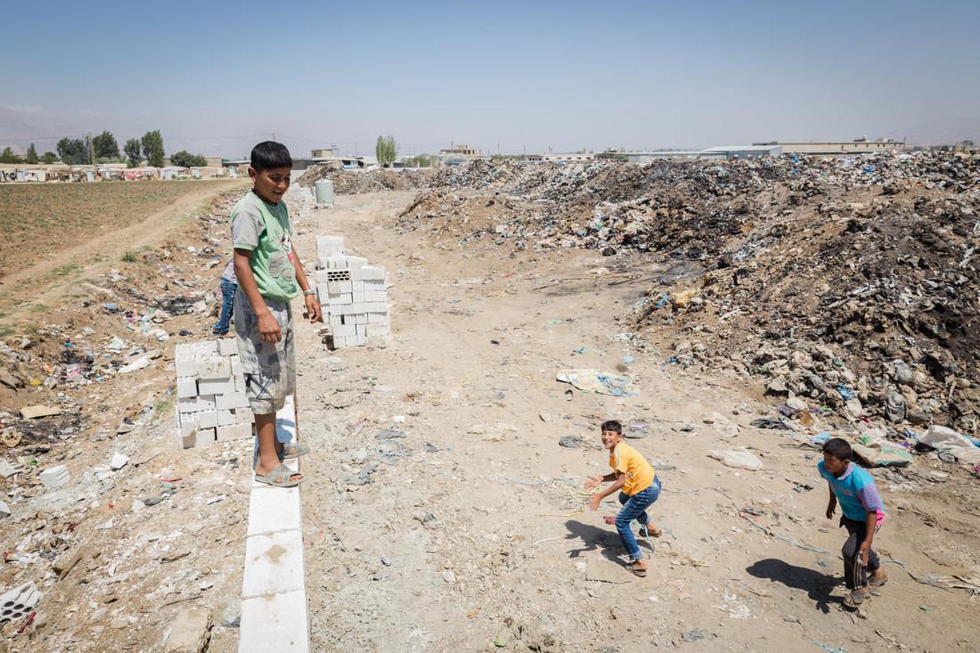 Bambini giocano vicino ad un muro, costruito da Oxfam Italia per separare da una discarica un insediamento con 400 profughi nella valle della Bekaa. 