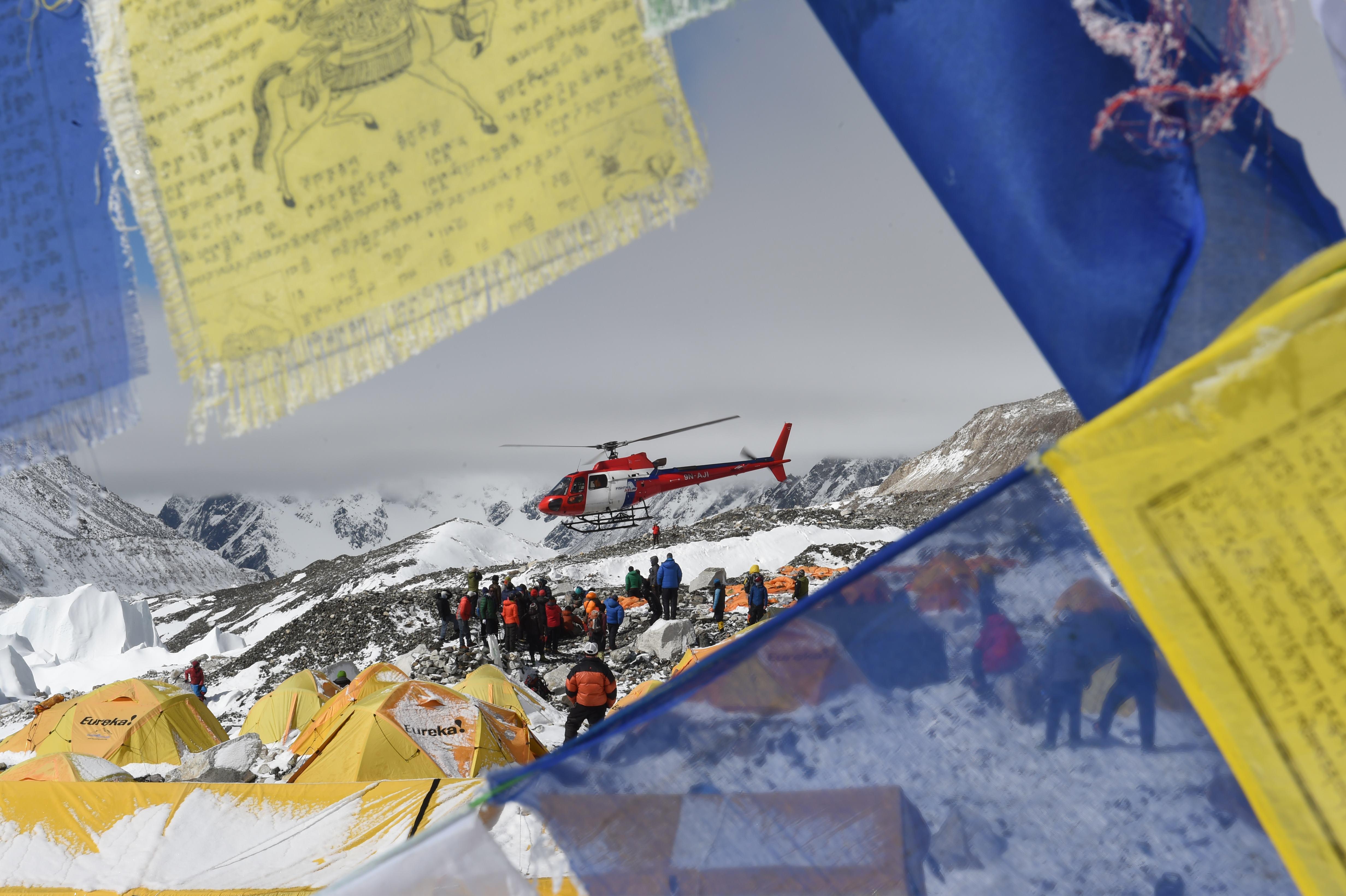 TOPSHOTS Prayer flags frame a rescue helicopter as it ferries the injured from Everest Base Camp on April 26, 2015, a day after an avalanche triggered by an earthquake devastated the camp. Rescuers in Nepal are searching frantically for survivors of a huge quake on April 25, that killed nearly 2,000, digging through rubble in the devastated capital Kathmandu and airlifting victims of an avalanche at Everest base camp. AFP PHOTO/ROBERTO SCHMIDT