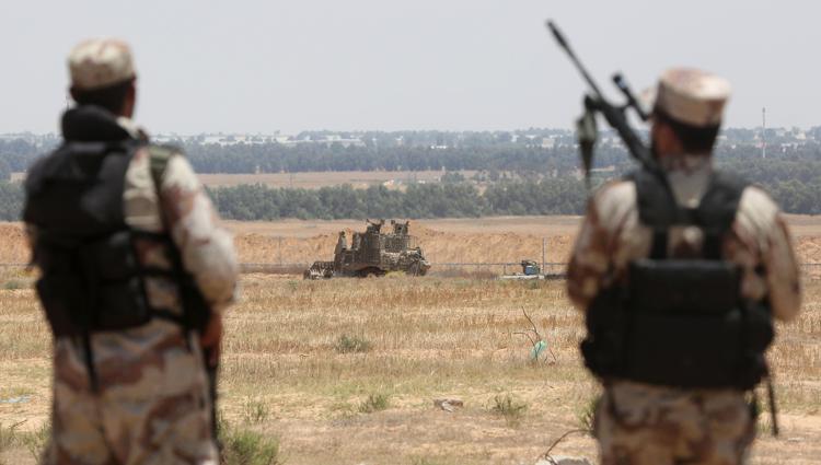 Militanti del braccio armato di Hamas a Gaza guardano bulldozer israeliano oltre il confine.  - (foto AFP)