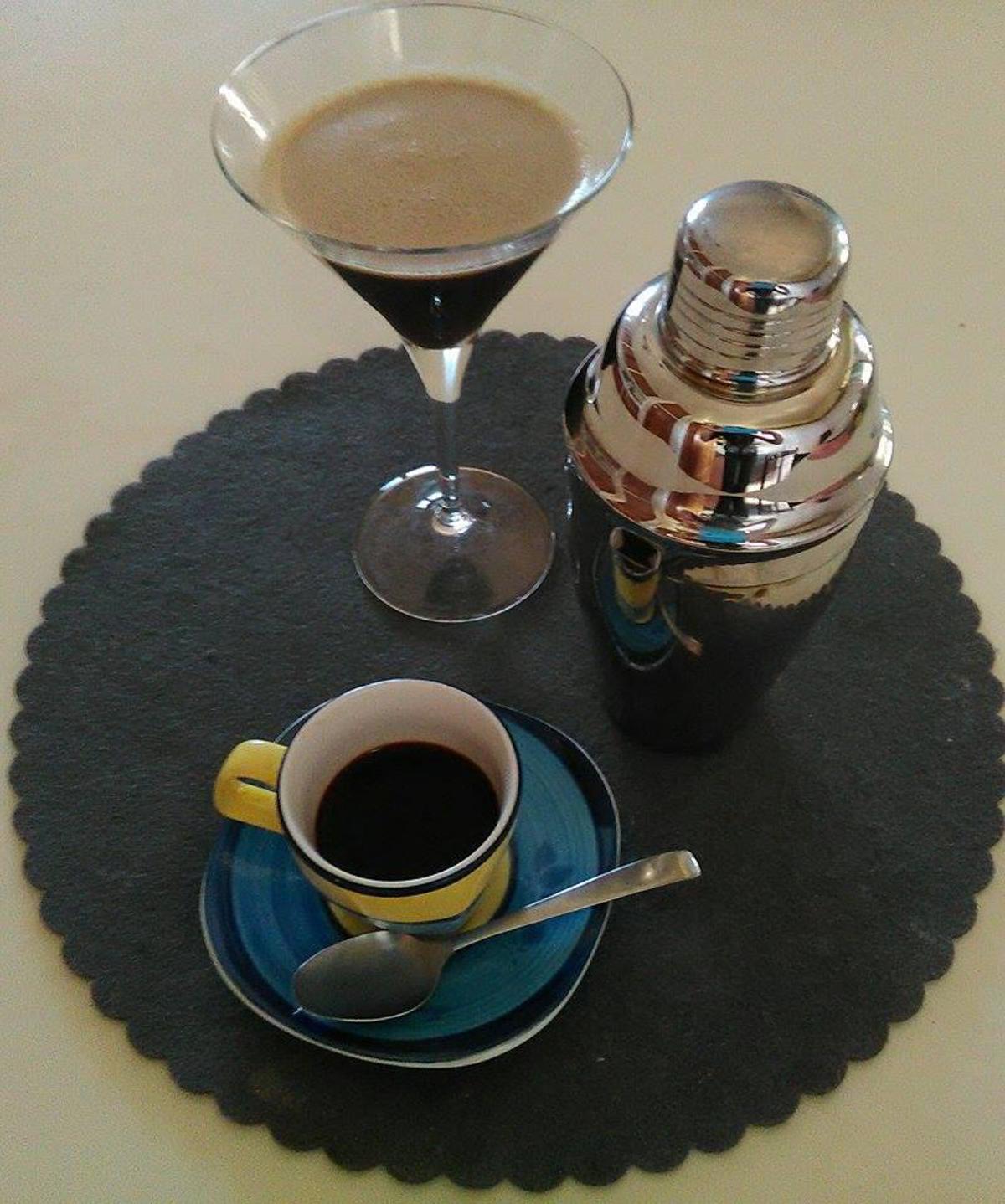 sul tavolo uno shaker una tazzina di caffè e una coppa per martini con il risultato finito
