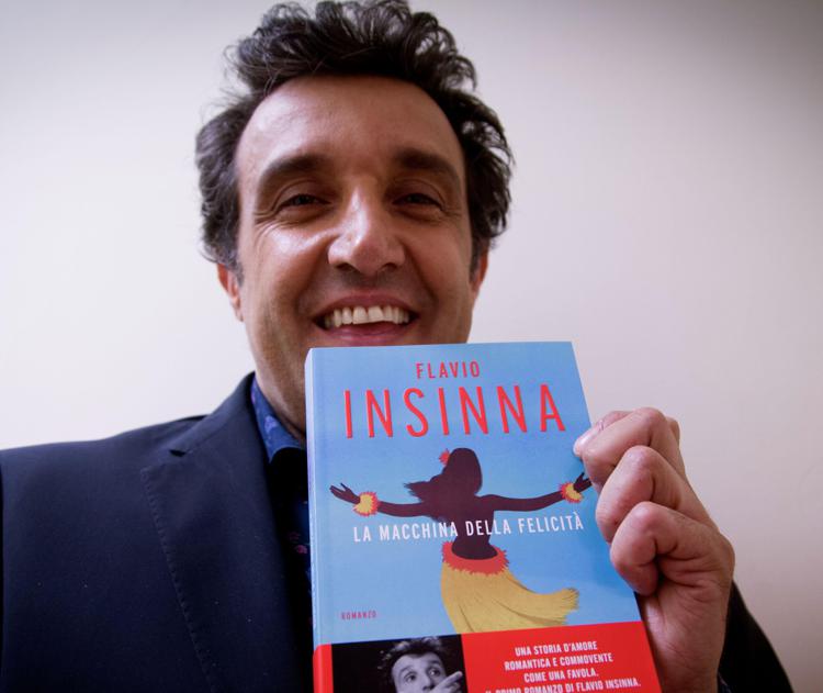 Il conduttore televisivo Flavio Insinna mostra sorridente il suo primo romanzo