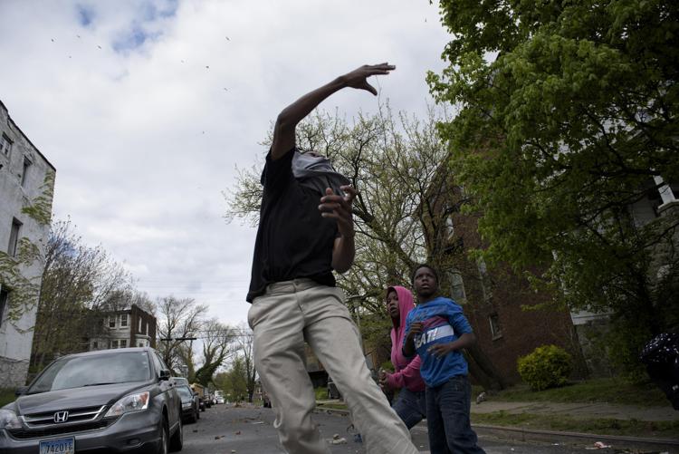 Un giovane che lancia una pietra contro polizia a Baltimora (Foto Afp) 