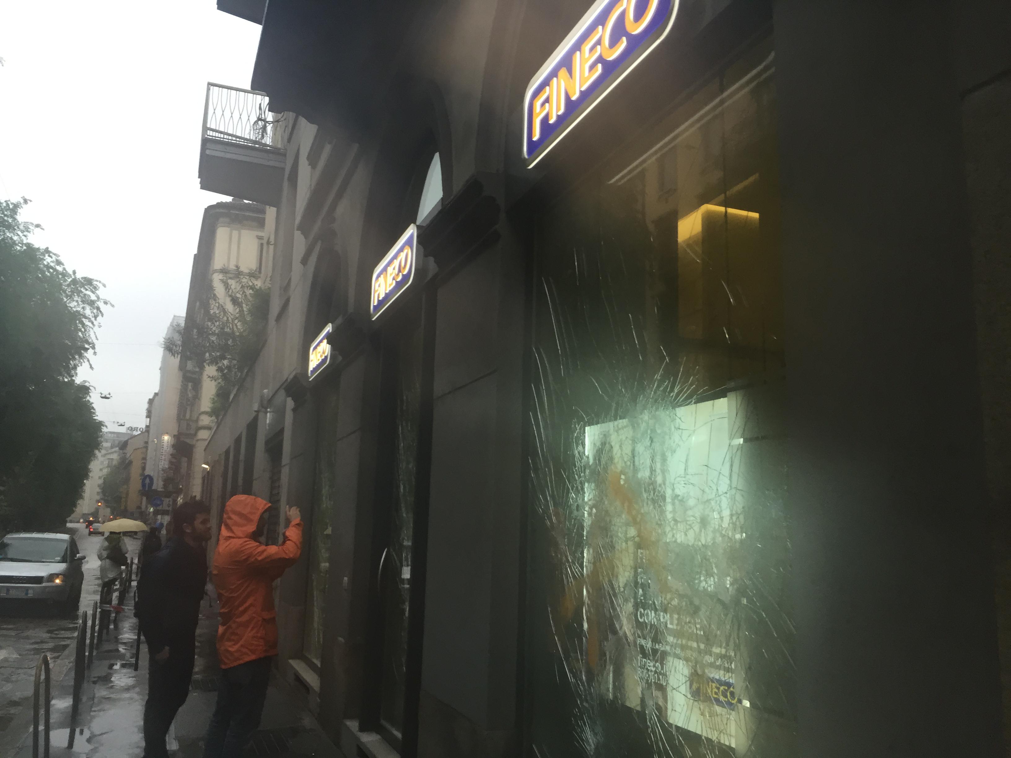 Alcuni passanti fotografano i danni dei manifestanti ai danni delle vetrine Fineco