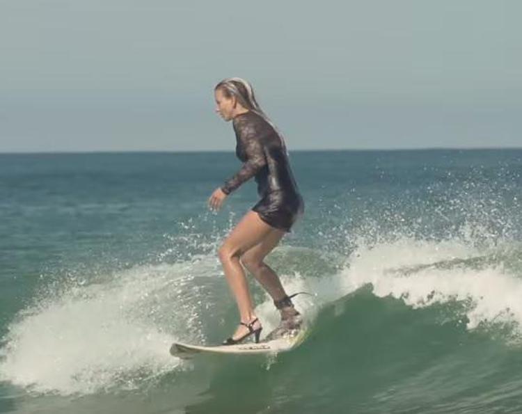 Tubino nero e tacchi alti, così la sexy surfista cavalca le onde/Video