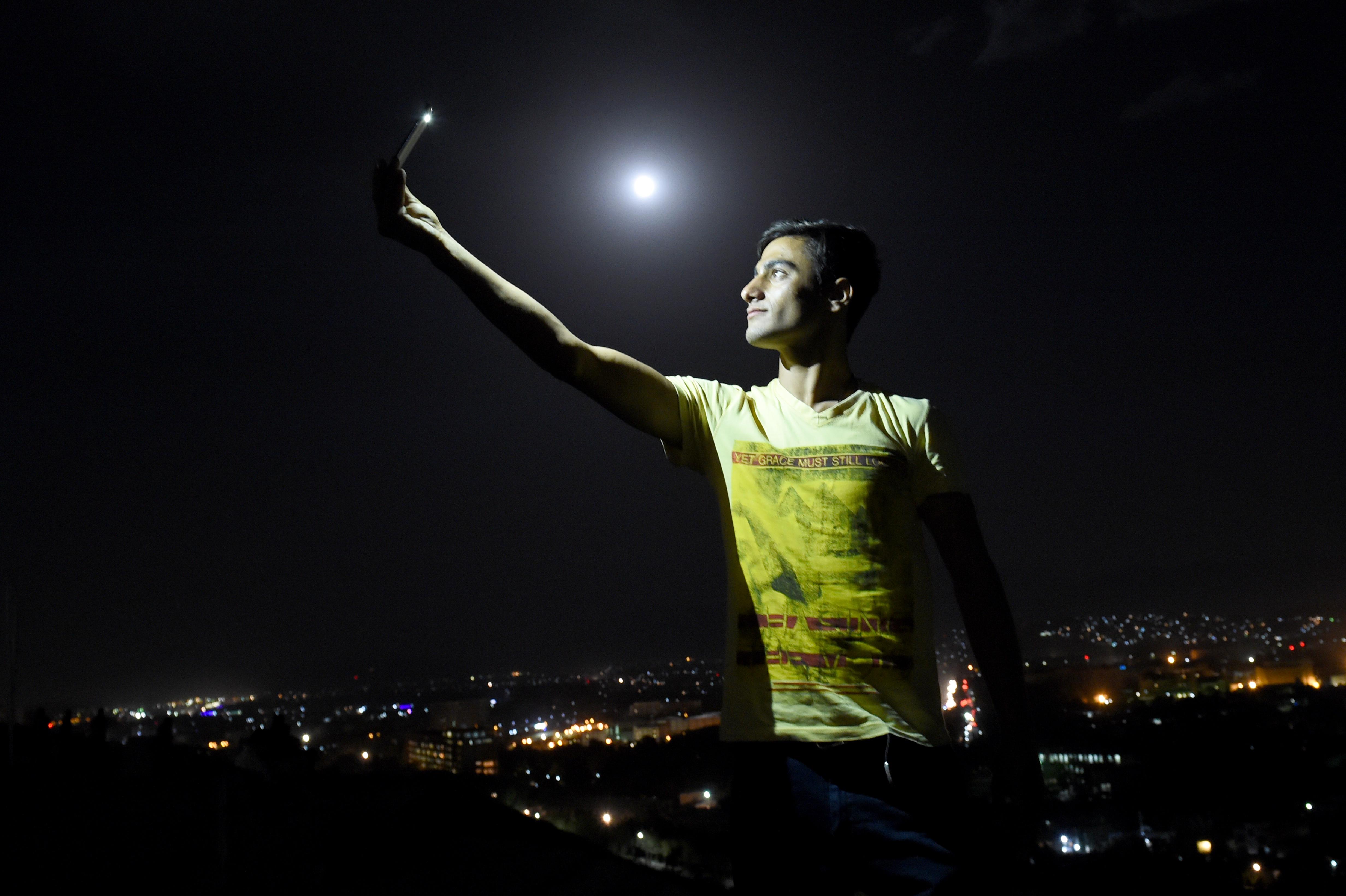 In questo foto, un uomo afgano è illuminato dalla luce dal suo telefono durante un selfie sulla cima della collina di Wazir Akbar Khan a Kabul, Afghanistan (AFP PHOTO / Wakil Kohsar)