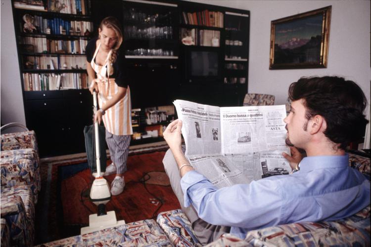 Una signora pulisce, mentre l'ospite legge il giornale (Fotogramma)