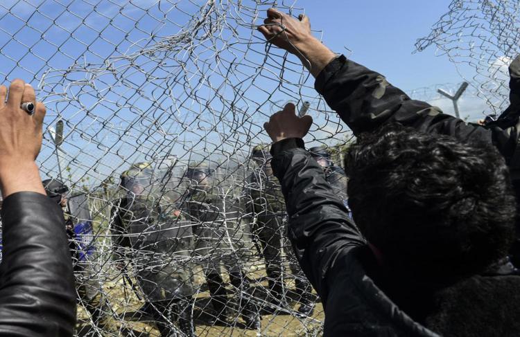 Migrants and refugees pull down the fence during clashes with Macedonian soldiers for the reopening of the border near their makeshift camp in the northern Greek border village of Idomeni, on April 10, 2016. Dozens of people were hurt when police fired tear gas on a group of migrants as they tried to break through a fence on the Greece-Macedonia border, the medical charity Doctors without Borders (MSF) said. A plan to send back migrants from Greece to Turkey sparked demonstrations by local residents in both countries days before the deal brokered by the European Union is set to be implemented. / AFP PHOTO / BULENT KILIC - AFP