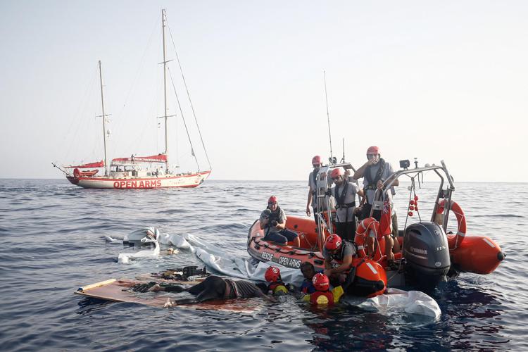 L'imbarcazione soccorsa a largo della Libia da Open Arms. Nell'immagine, il salvataggio dell'unica superstite e il corpo di una delle vittime (Afp)