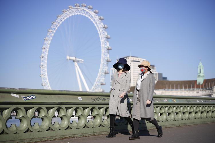 Pedestrians in masks walk along Westminster Bridge with the London Eye in the backgroud, in a quiet central London on March 25, 2020, after Britain's government ordered a lockdown to slow the spread of the novel coronavirus. - Britain was under lockdown, its population joining around 1.7 billion people around the globe ordered to stay indoors to curb the 