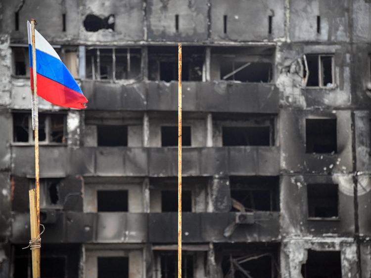 La bandiera della Russia davanti a un edificio distrutto di Mariupol