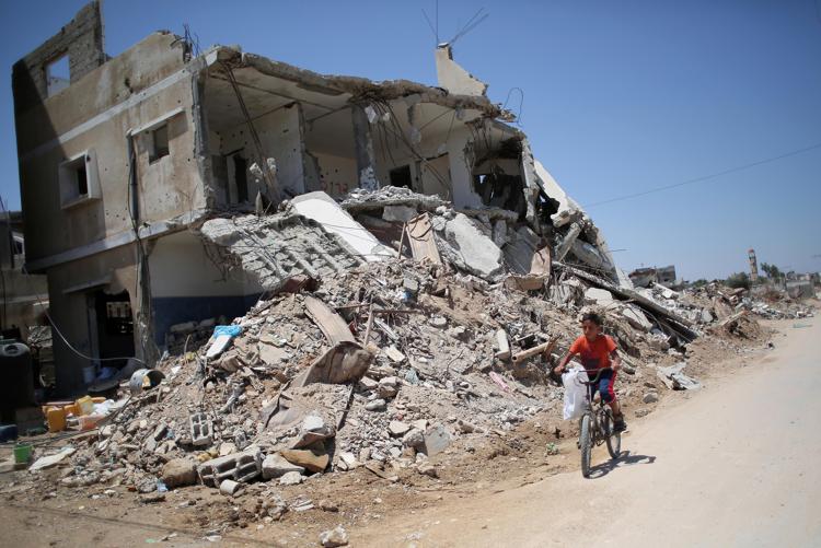 TOPSHOTS A Palestinian boy rides his bicycle past buildings which were destroyed AFP PHOTO / SAID KHATIB - AFP
