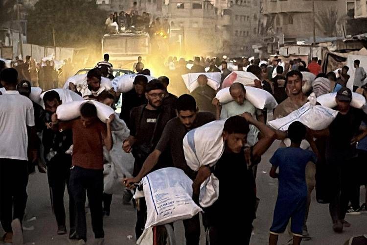 Uomini camminano con sacchi di farina presi da un camion razziato che trasportava derrate alimentari, a Khan Yunis nel sud della striscia di Gaza - (Afp)