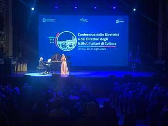 Palco con artisti italiani in concerto, bandiere europee sullo sfondo, pubblico in sala da spettacolo, immagine di approfondimento