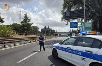 Fiamme nella macchia mediterranea con elicotteri in volo, turisti in spiaggia durante evacuazione, traffico bloccato su strada urbana, immagine di approfondimento
